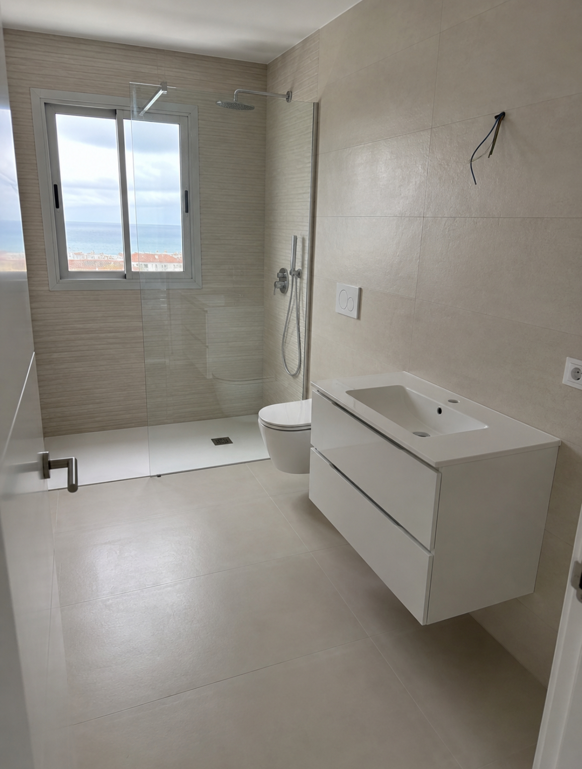Bagno con mobile lavabo sospeso, WC sospeso e doccia con vista mare